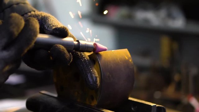 Shooting of grinding of a metal part by a master in protective gloves
