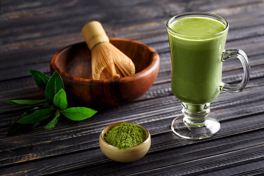 Matcha green tea latte beverage in glass cup on dark wooden background