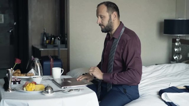 Young businessman finishing work on laptop during breakfast in hotel
