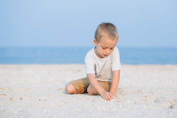 Fototapeta na wymiar Portrait smiling little boy playing in the sand near the sea, ocean. Positive human emotions, feelings, joy. Funny cute child making vacations and enjoying summer.