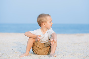Fototapeta na wymiar Serious cute little boy near water at the beach on hot summer day. Having fun during vacation..