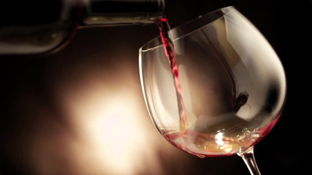 Wine. Red wine pouring in wine glass over dark background. Slow motion 4K UHD video 3840x2160