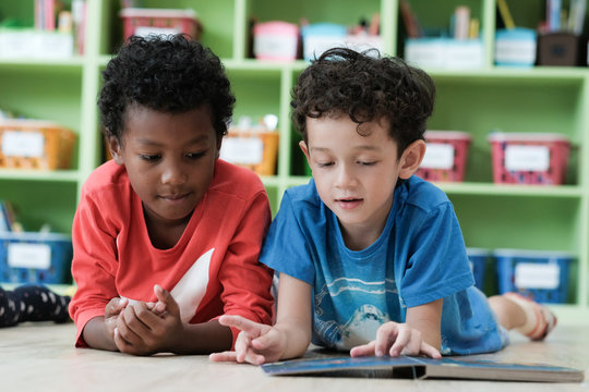 American and African boys are reading together with happiness in their kindergarten classroom, kid education concept