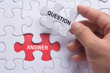 Hand holding piece of jigsaw puzzle with word question & answer.