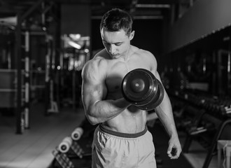 Fototapeta na wymiar Muscular young bodybuilder training in gym, black and white effect