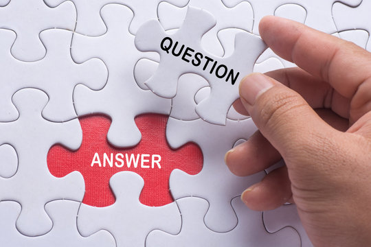 Hand holding piece of jigsaw puzzle with word question & answer.