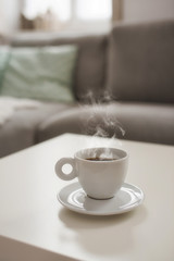 Still life details in home interior of living room. Sweaters and cup of coffe with steam on a serving tray on a coffee table. Breakfast over sofa in morning sunlight.