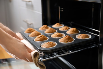 Woman taking baking tray with cupcakes from oven - Powered by Adobe