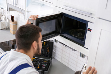 Young man repairing microwave oven in kitchen