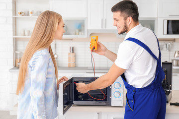 Housewife with worker near microwave oven in kitchen