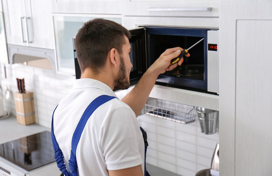 Young man repairing microwave oven in kitchen