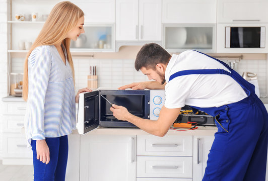 Housewife with worker near microwave oven in kitchen