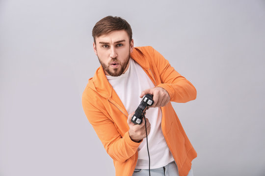 Emotional man with video game controller on grey background