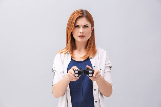 Emotional woman with video game controller on grey background