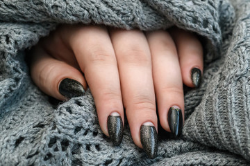 Beautiful winter manicure. Black lacquer with luster and white patterns of snow and frost. The gray background is also with beautiful curled drawings