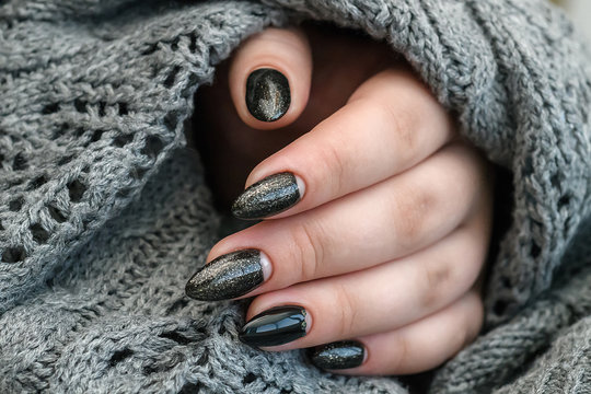 Beautiful winter manicure. Black lacquer with luster and white patterns of snow and frost. The gray background is also with beautiful curled drawings