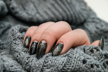 Beautiful winter manicure. Black lacquer with luster and white patterns of snow and frost. The gray background is also with beautiful curled drawings