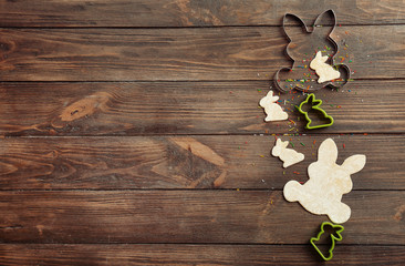 Bunny shaped cookie cutters and raw dough on wooden background. Easter celebration