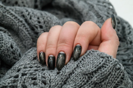 Beautiful winter manicure. Black lacquer with luster and white patterns of snow and frost. The gray background is also with beautiful curled drawings
