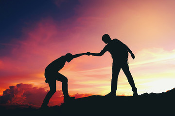 Teamwork couple helping hiking each other silhouette on mountains