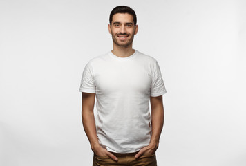 Young european man standing with hands in pockets, wearing blank white tshirt with copy space for...
