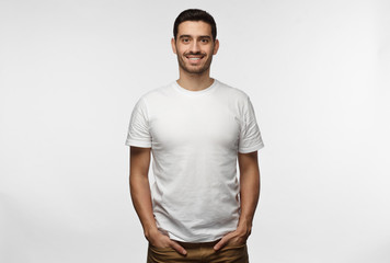 Young european man standing with hands in pockets, wearing blank white tshirt with copy space for...