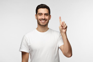 Attractive young man in white t-shirt pointing up with his finger isolated on gray background
