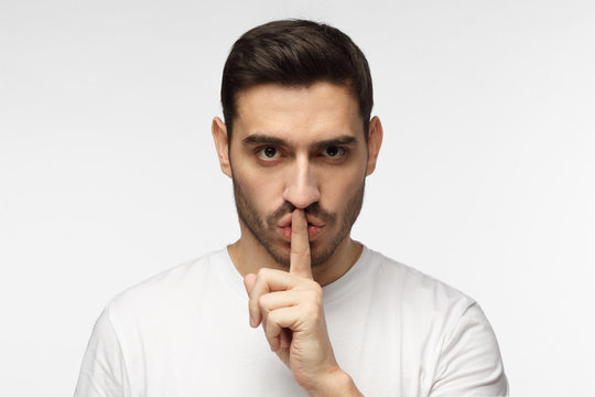 Close up shot of handsome strict man with shh gesture, asking for silence or to be quiet, isolated on gray background