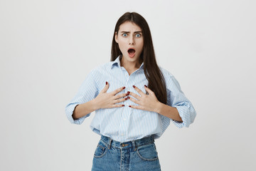 Portrait of shocked and insulted european woman, holding hands on breast with opened mouth and...