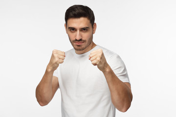 Confident sporty man in white t-shirt holding fists in front of him going to fight and defend himself. Handsome athletic male showing his strength, ready for challenges
