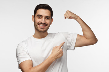 Young strong sporty athletic man in white t-shirt, shows biceps after training in gym, isolated on...