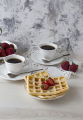 on a light background a cup of coffee and waffles with strawberries