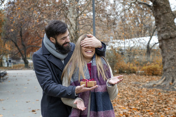 Young couple in park on date and he is giving a present to her