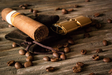 Close-up of cigar and lighter with coffee beans on rough wood
