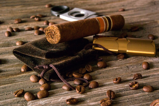 Close-up of cigar, lighter and guillotine with coffee beans on rough wood