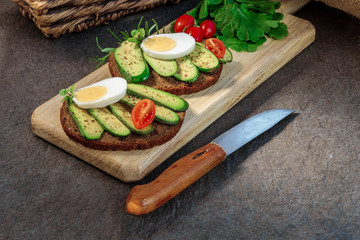 Sandwich with seedless avocado, egg and cherry tomato on the cutting board, knife is near. Avocado without any seed. Cocktail avocado. Cucumber avocado.