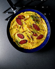 Crepes mit Salamischeiben und Lauchzwiebeln in blauer Pfanne