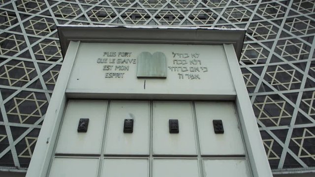 Tilt up to the Grande synagogue de la Paix on a rainy day and quote in French and Hebrew - Plus fort que le glaive est mon esprit quote.