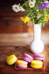 A cup of hot black coffee and bright macaroons on a wooden table at dark background with colorful bokeh
