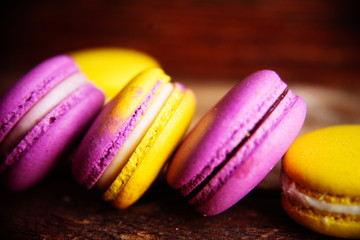 Colored macaroons pastel colors with different flavors on glass plate with paper towel. Bright and delicious dessert/ Wooden background