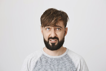 Fototapeta premium Indoor portrait of disappointed unsatisfied bearded european man looking at his messy hair with dislike, standing over gray background. Maybe I should finally call barber to make appointment