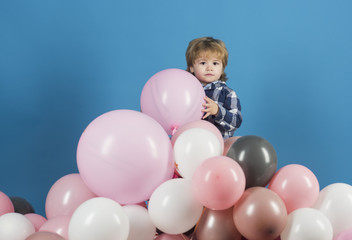 Fototapeta na wymiar Boy kid and mountain of pink balloons, birthday holiday or opening new children shop or kindergarten. Game and good mood, child holding keeps ball toy. Cute boy with long hair played in playground