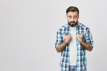 Studio shot of bearded european person pointing at himself with offended expression, standing...