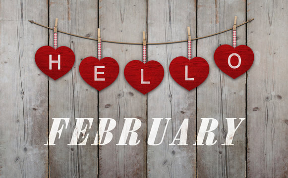 Hello february written on hangingred hearts and weathered wooden background