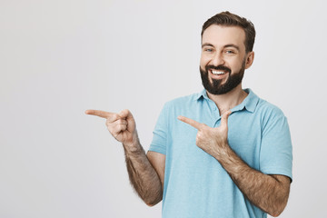 Portrait of a caucasian smiling bearded handsome man poiting at side isolated on a white background. Guy is telling his friends that he will be back with drinks in a minute.