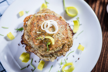 stacked fried potato cakes on white plate with sour cream, spring onion and chives