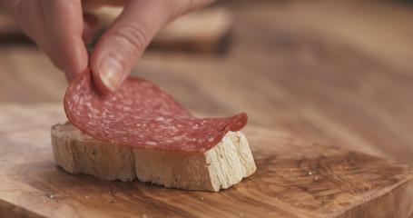 female hand make sandwich baguette slice with cream cheese and salami