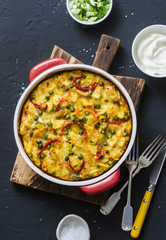 Potatoes and vegetables tortilla on a dark background, top view. Potatoes, green beans, bell peppers, green peas, cheese, eggs casserole in a baking dish -  delicious breakfast or snack