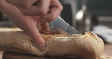 closeup slicing fresh baguette on cutting board