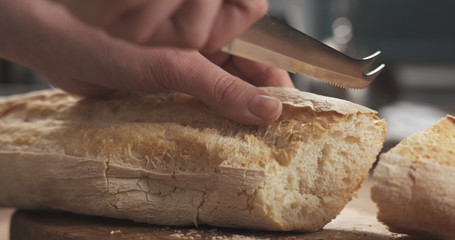 closeup slicing fresh baguette on cutting board
